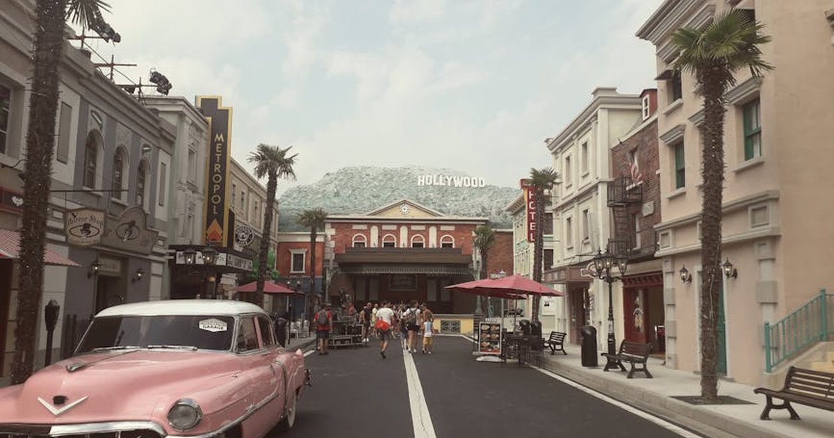 A vintage street scene featuring a pink classic car and Hollywood sign in an urban setting.