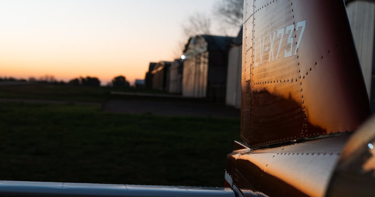 A close-up of an airplane tail reflecting sunset hues by an aircraft hangar.
