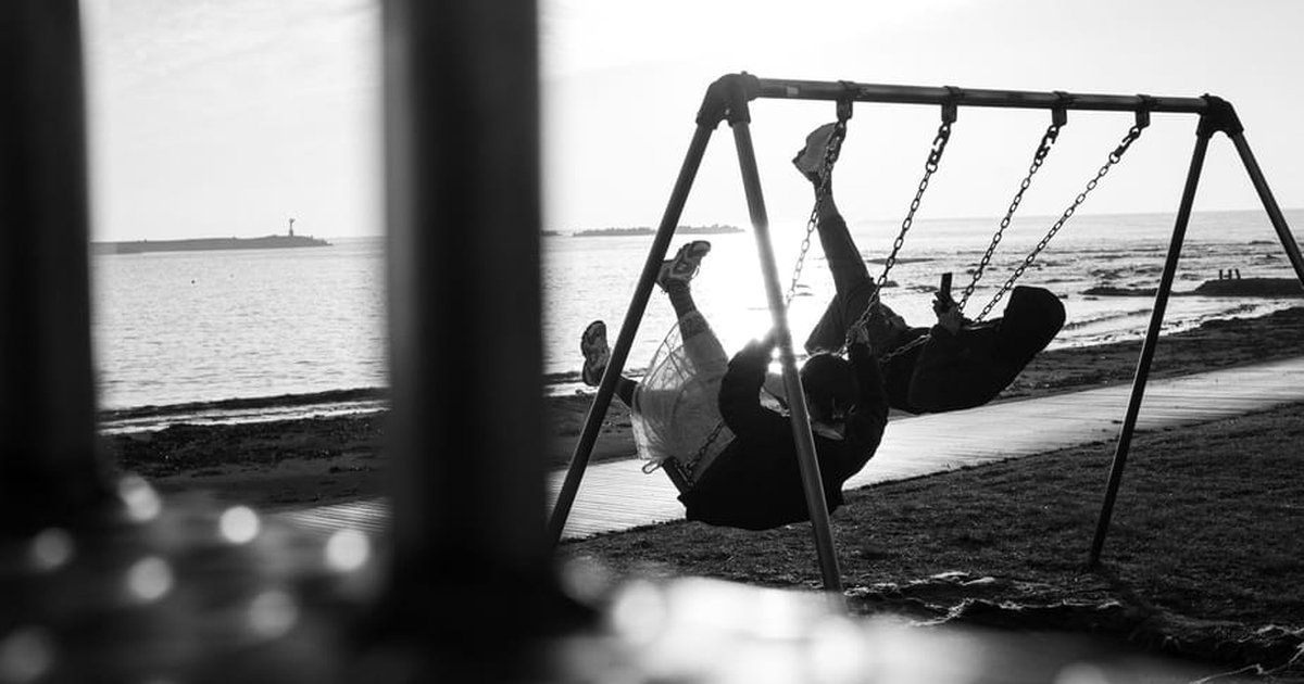 A couple enjoys swinging together by the seaside, capturing joyful moments in black and white.
