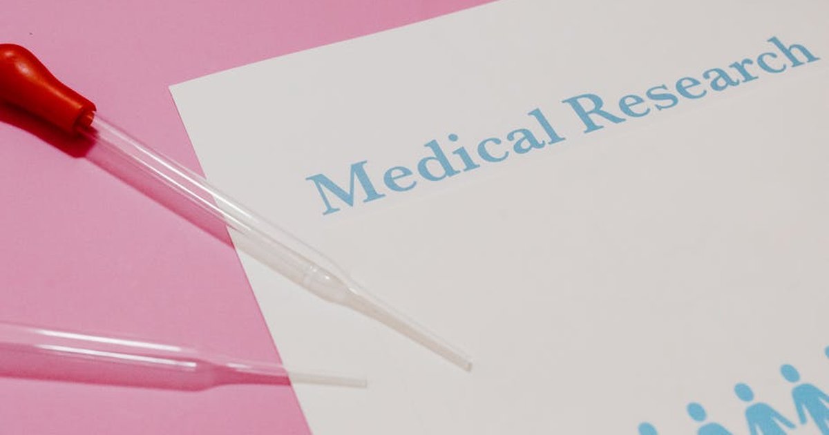 Close-up of a medical research document and pipette on a pink surface, highlighting scientific research and healthcare.