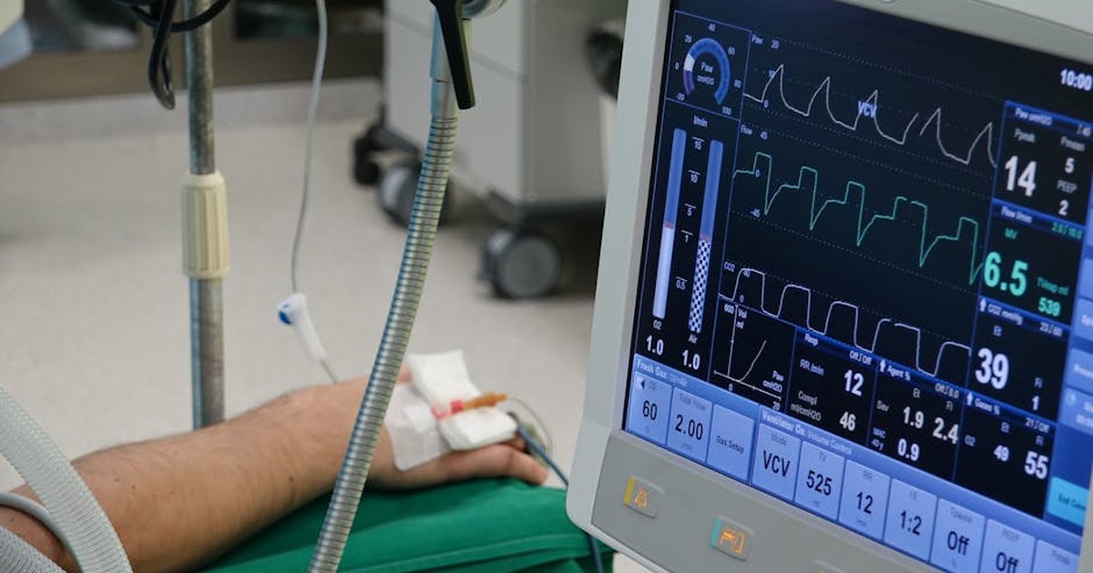 A close-up of a patient's hand connected to medical equipment in an ICU room.