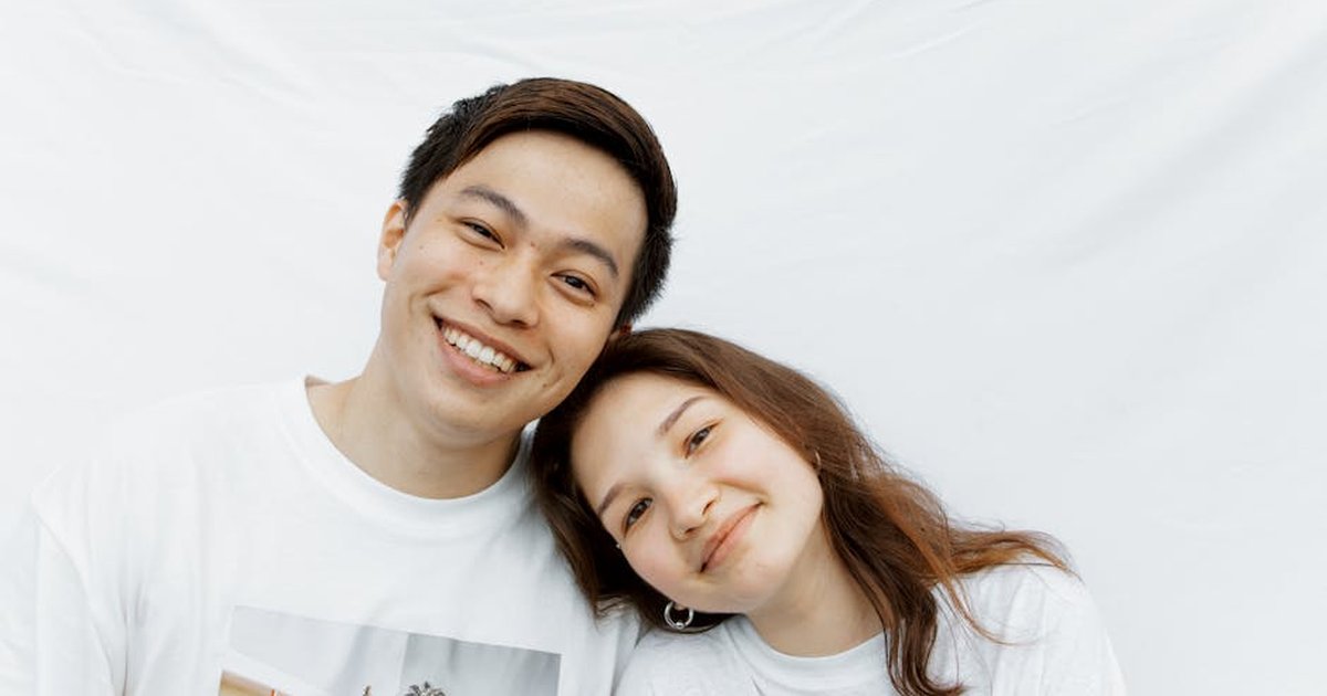 A cheerful young couple smiling and posing closely against a white background.