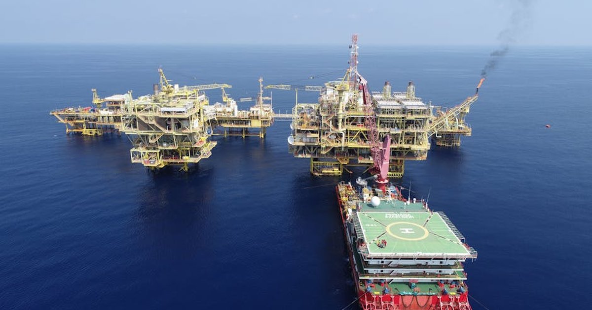 Aerial shot of multiple offshore oil platforms in a serene, blue sea under clear skies.