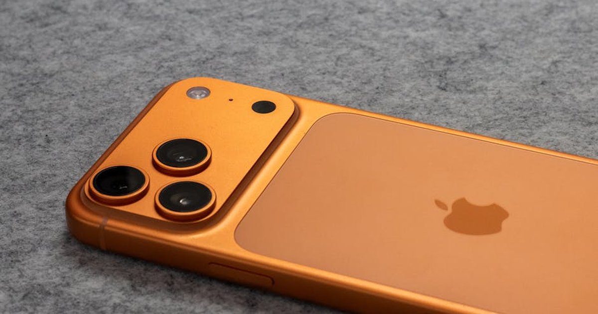 Orange smartphone with dual cameras placed on a soft gray fabric surface.
