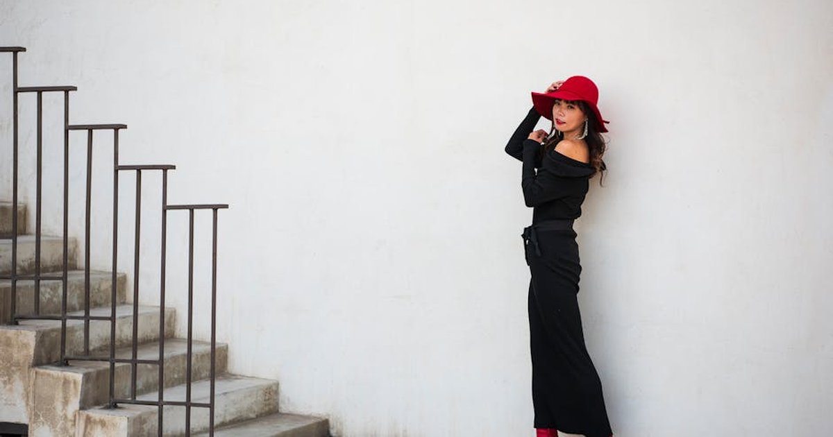 Elegant woman in a black dress and red hat standing by stairs, exuding modern style.