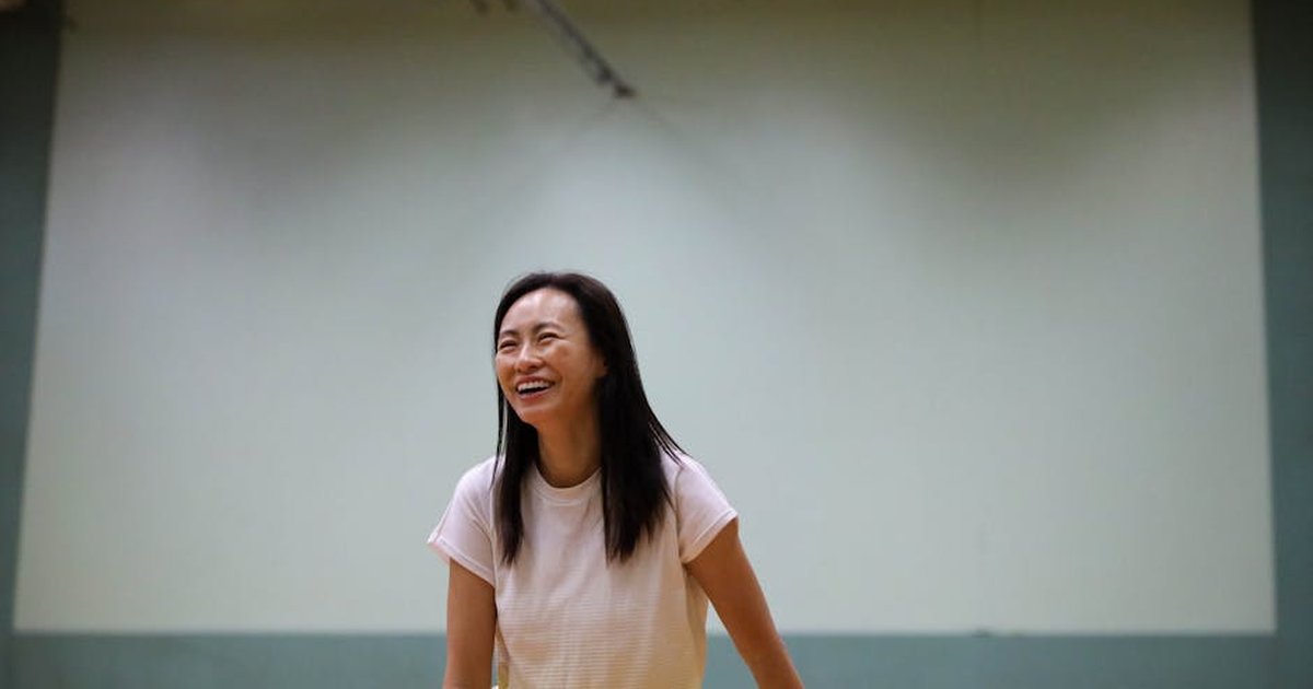 A cheerful woman enjoys playing badminton indoors, showcasing an active lifestyle in a gym environment.