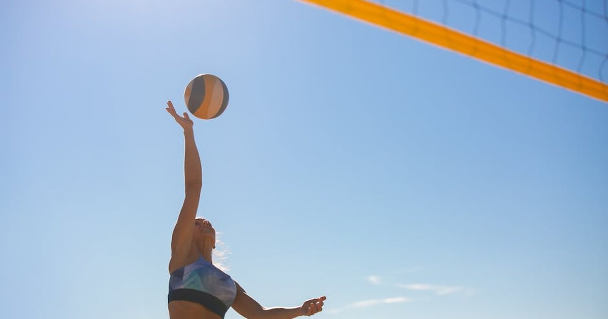 A woman spiking a volleyball on a sunny beach with a clear blue sky.