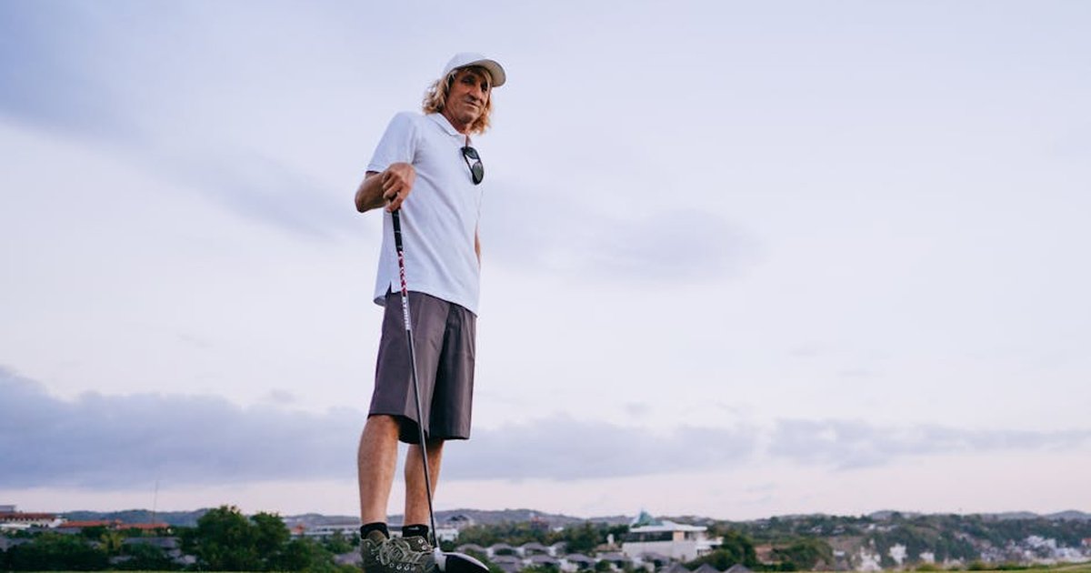 A man enjoying golf on a scenic course, under a clear sky, wearing relaxed attire.