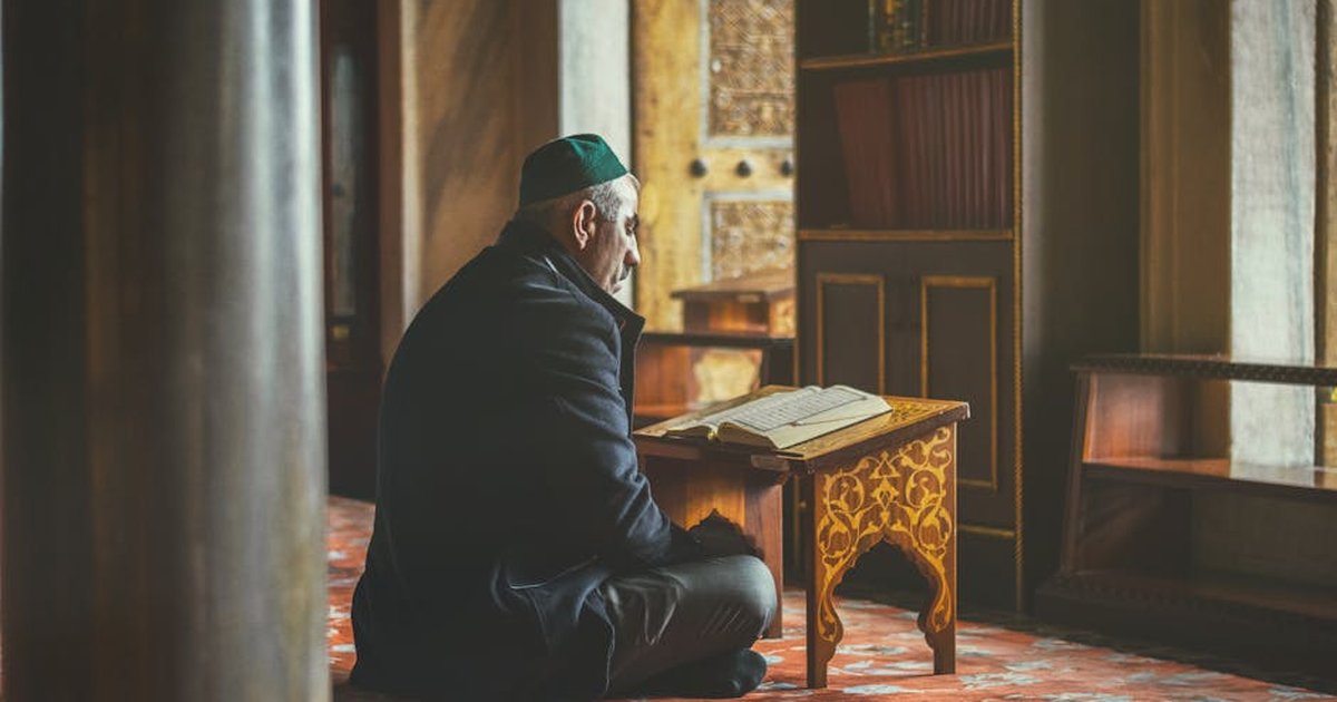 Elderly man reading Koran, seated in a historic Istanbul mosque, reflecting spirituality and contemplation.