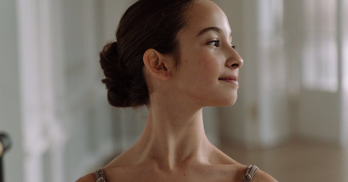 Side view portrait of a young ballet dancer looking serene in a softly lit indoor studio.