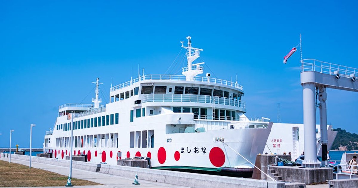 A bright white ferry with red dots docked at a pier under a clear blue sky.