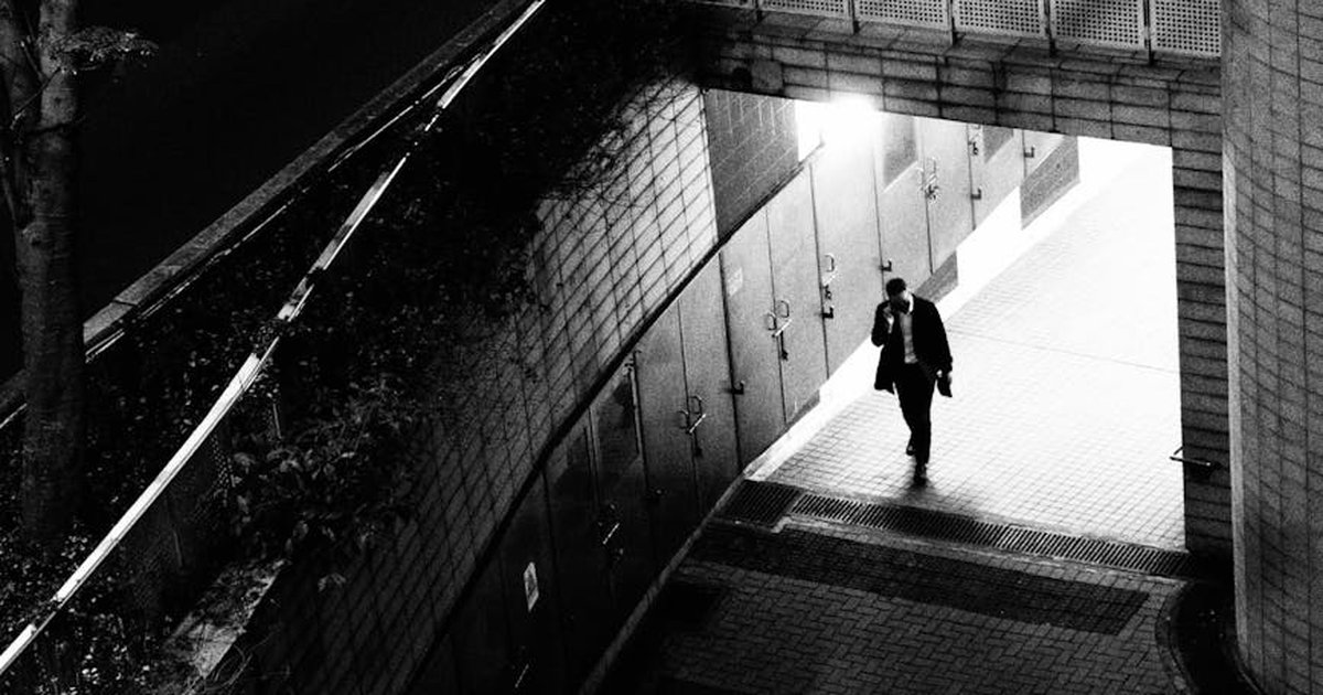 Black and white photo capturing a lone man walking in a moody urban setting in Hong Kong.