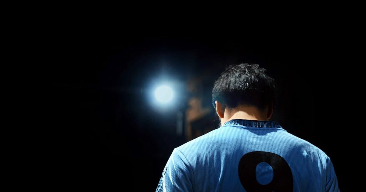 A soccer player in a blue jersey with number 9, illuminated by a spotlight at night.