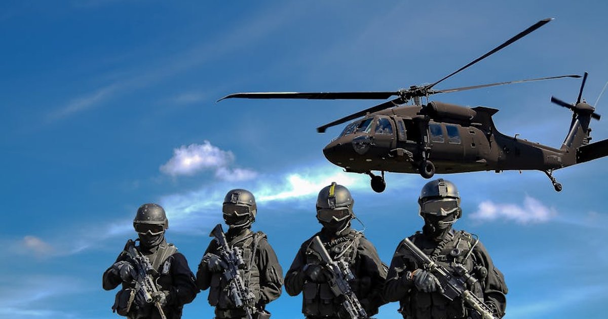 Special forces soldiers in tactical gear with helicopter overhead under a blue sky.