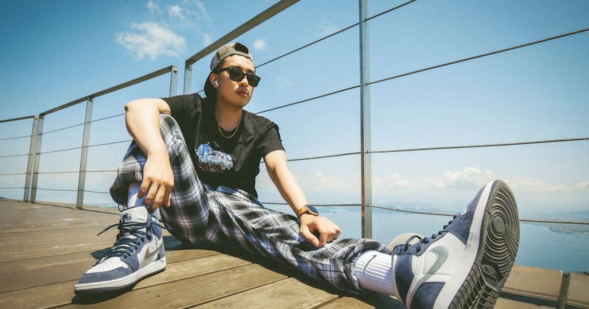 Young man in casual streetwear relaxes outdoors with scenic view.