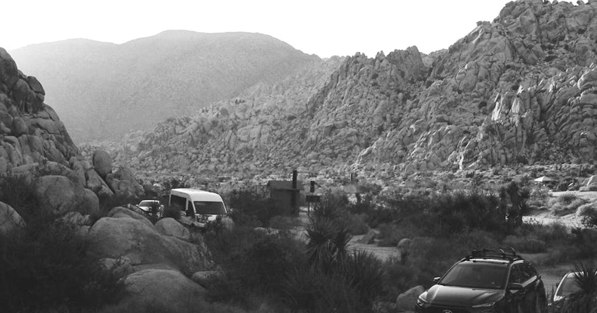 Black and white image of rocky landscape and vehicles at Joshua Tree National Park.