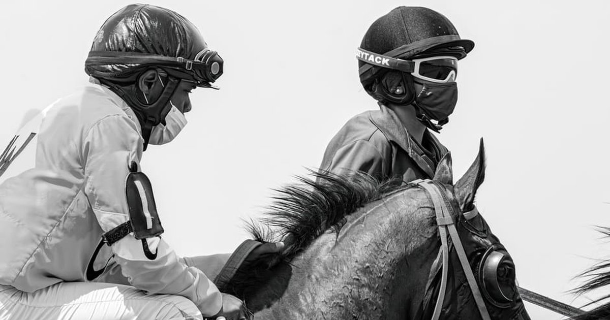 Two jockeys on horses, in black and white, during a race.