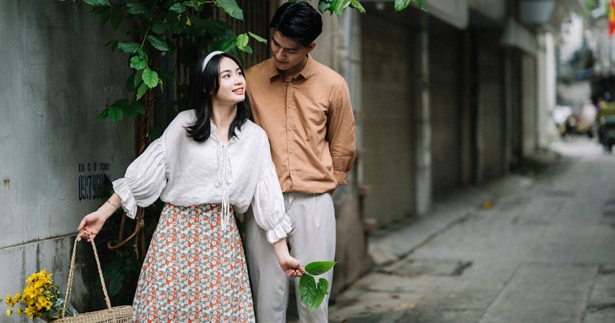 Young couple enjoying a casual stroll on a city street, surrounded by lush greenery.