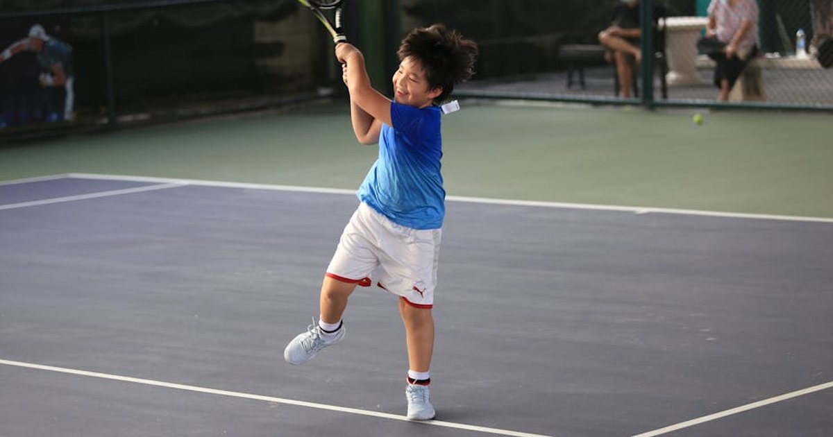A young boy enthusiastically plays tennis on an outdoor court in Bangkok, showcasing his skills.