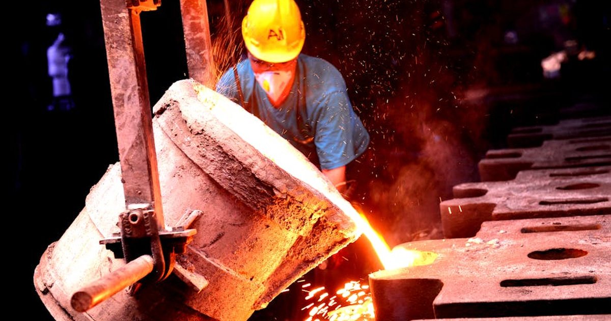 A factory worker wearing a helmet pours molten metal into molds, showcasing industrial metal casting.
