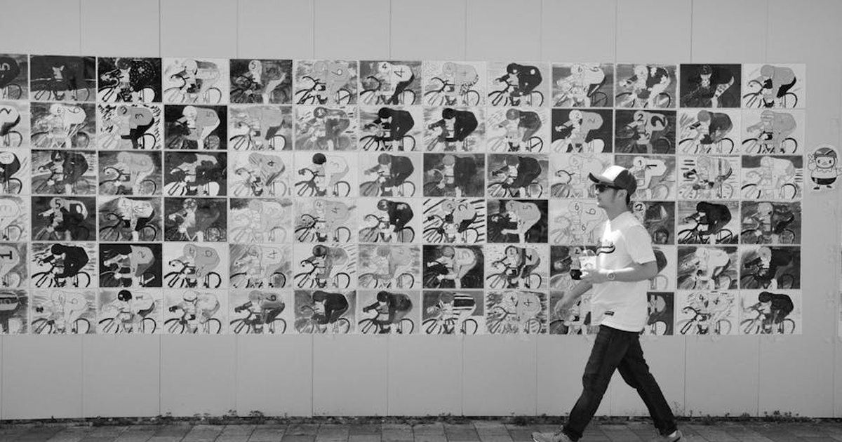 Black and white photo of a man walking past a detailed mural of cyclists.