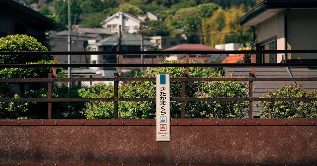 A sign at Kita Kamakura station, surrounded by lush greenery, under a clear sky in Japan.
