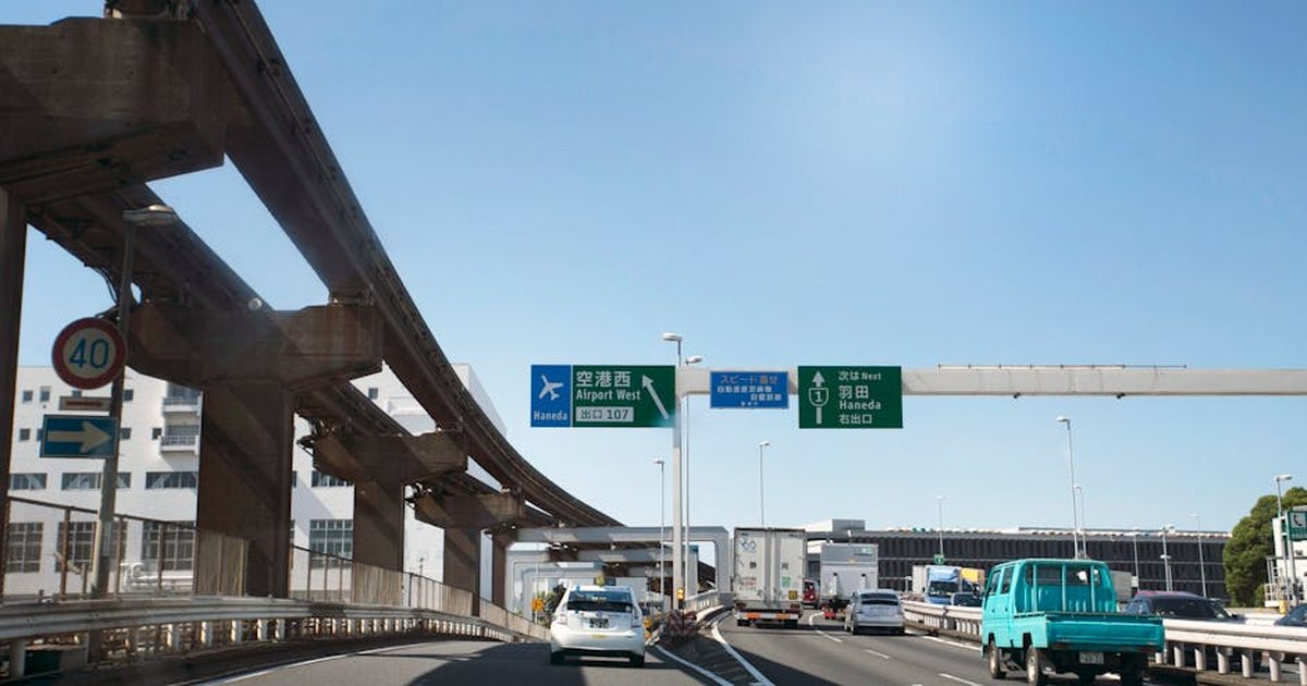 Cars on highway with signs towards Haneda Airport on a clear day in Tokyo.