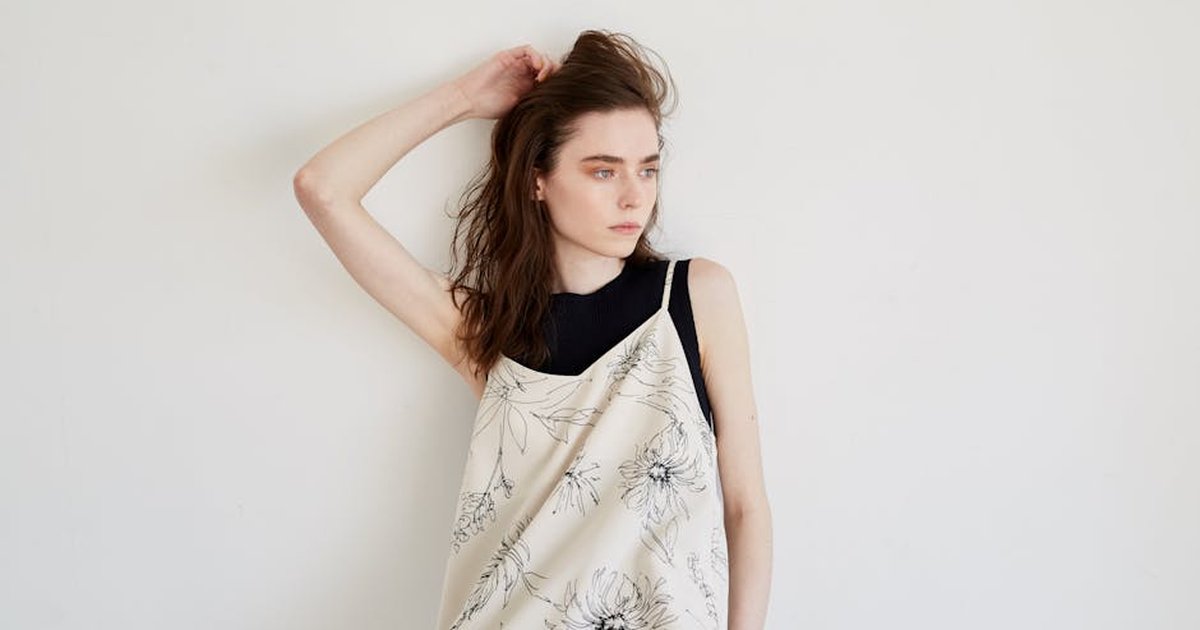 A thoughtful woman in a floral dress with hand in hair, offering copy space.