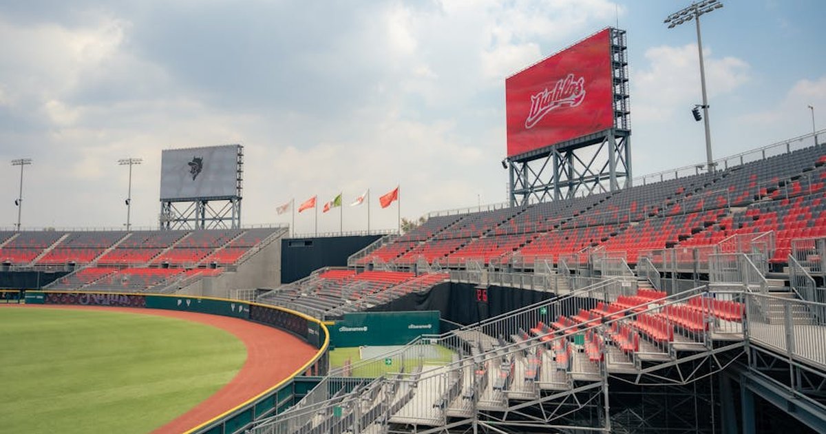 Wide-angle view of empty baseball stadium with red seats and clear sky.