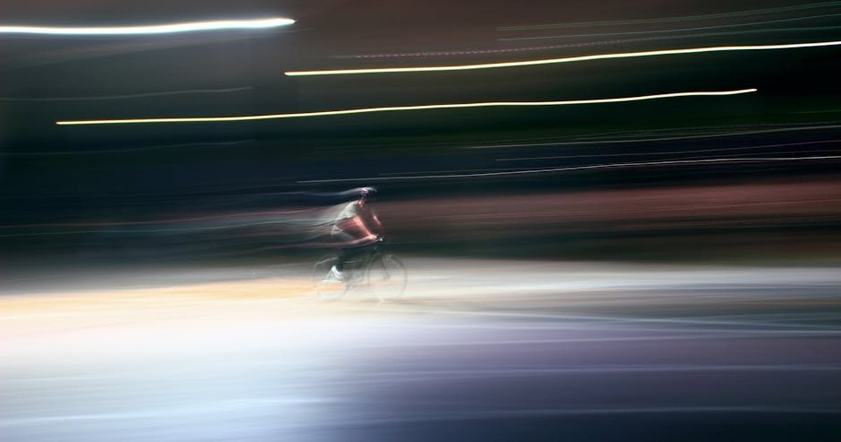 Blurred motion image of a cyclist riding at night, capturing speed and dynamism.