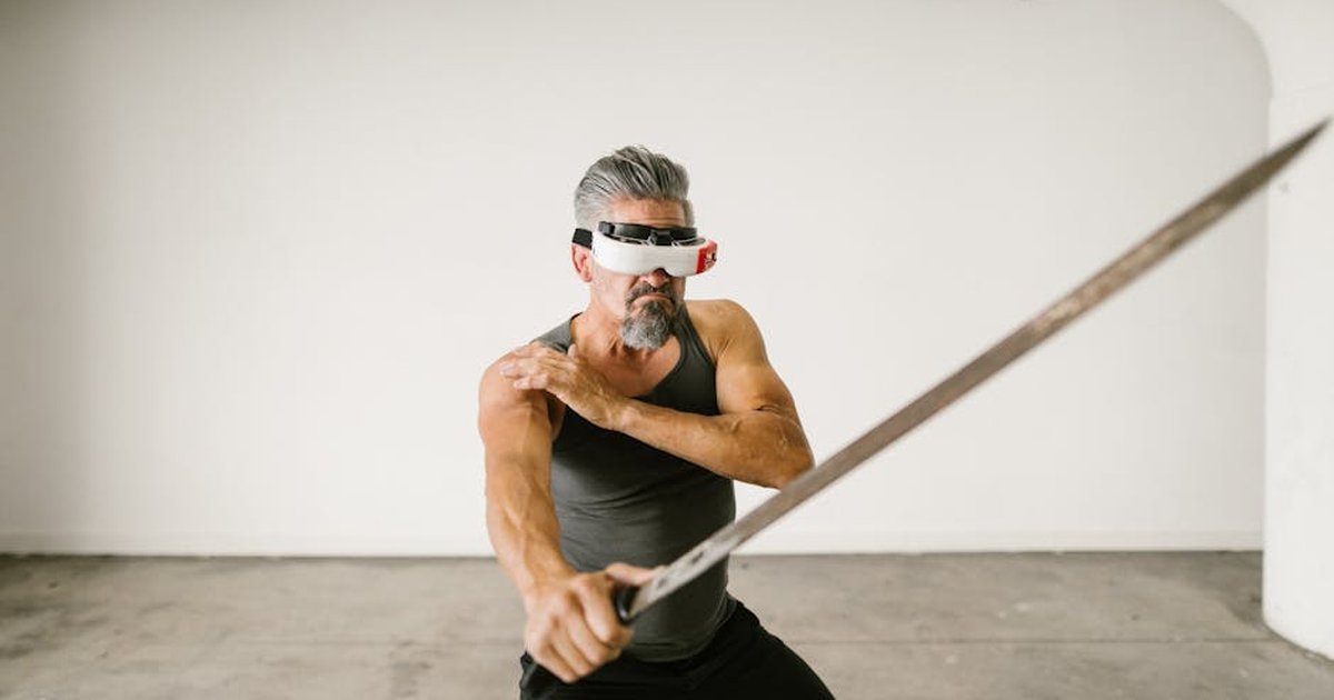 Adult man wearing VR headset practicing sword techniques in empty indoor space.