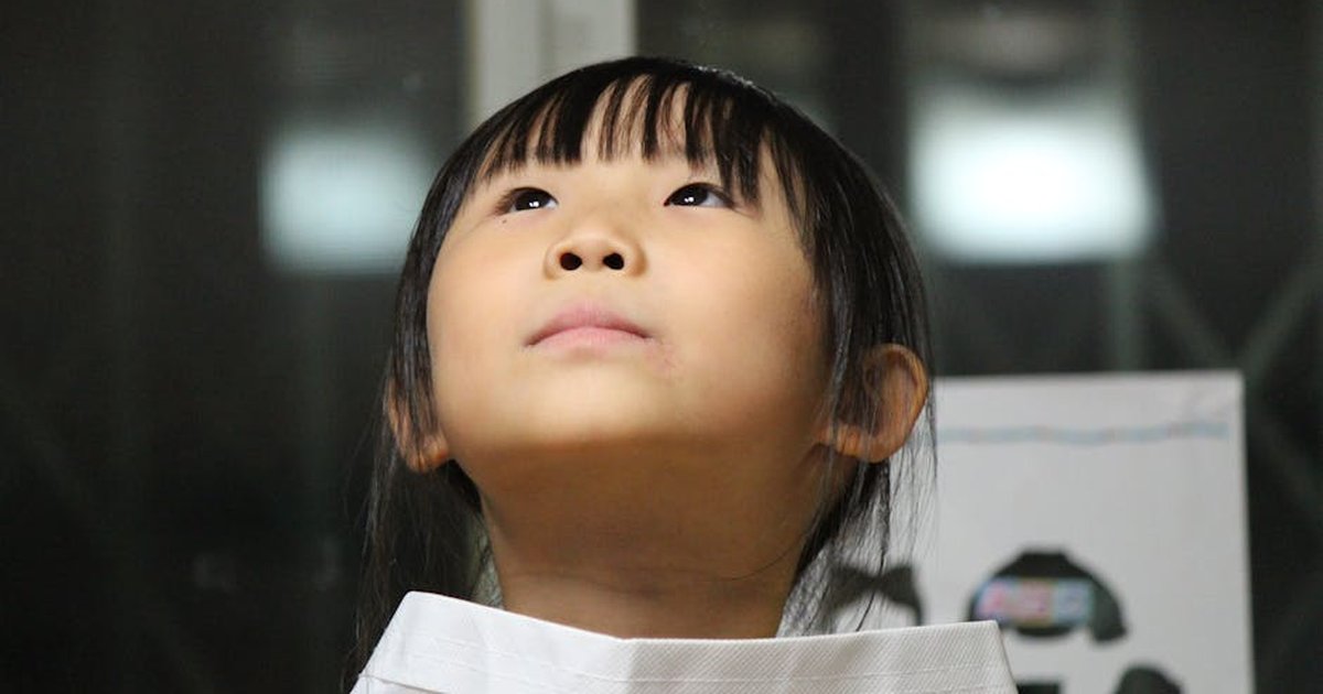 A young girl with an expression of curiosity looking up indoors, with a soft lighting background.