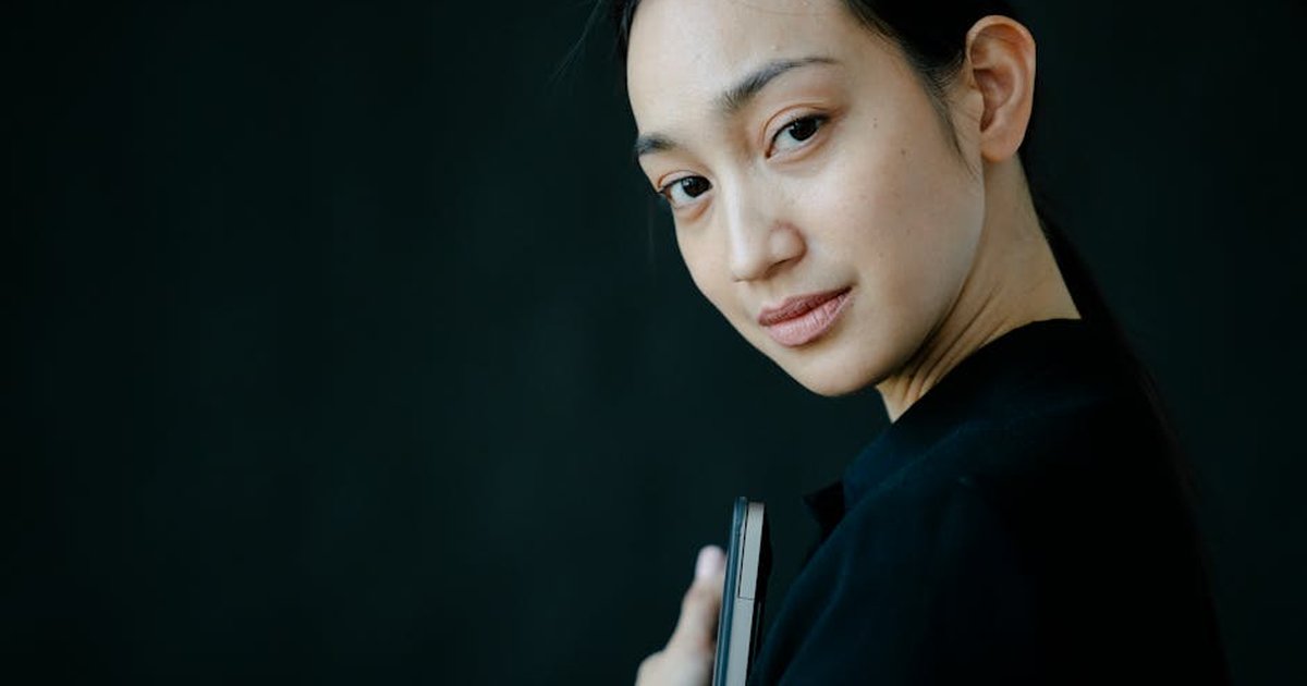 Studio portrait of an Asian woman looking thoughtful against a dark background.