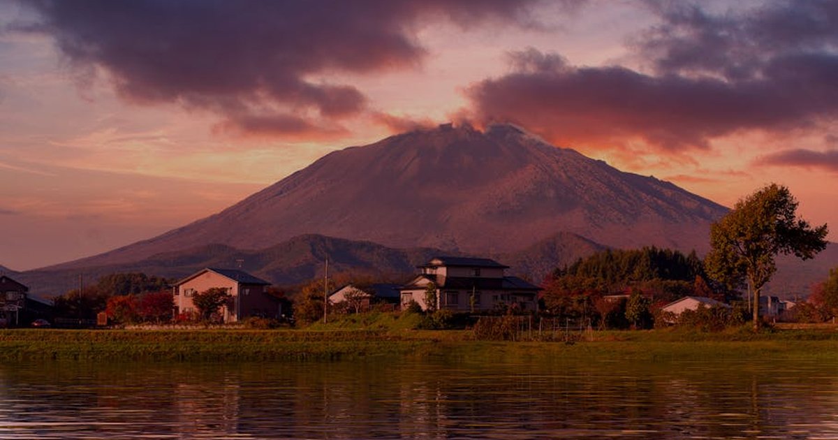 A serene landscape with a mountain and village at sunset, reflecting in a calm lake.