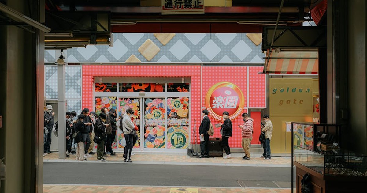 People lining up outside a colorful store in an Asian city, captured from a busy street setting.