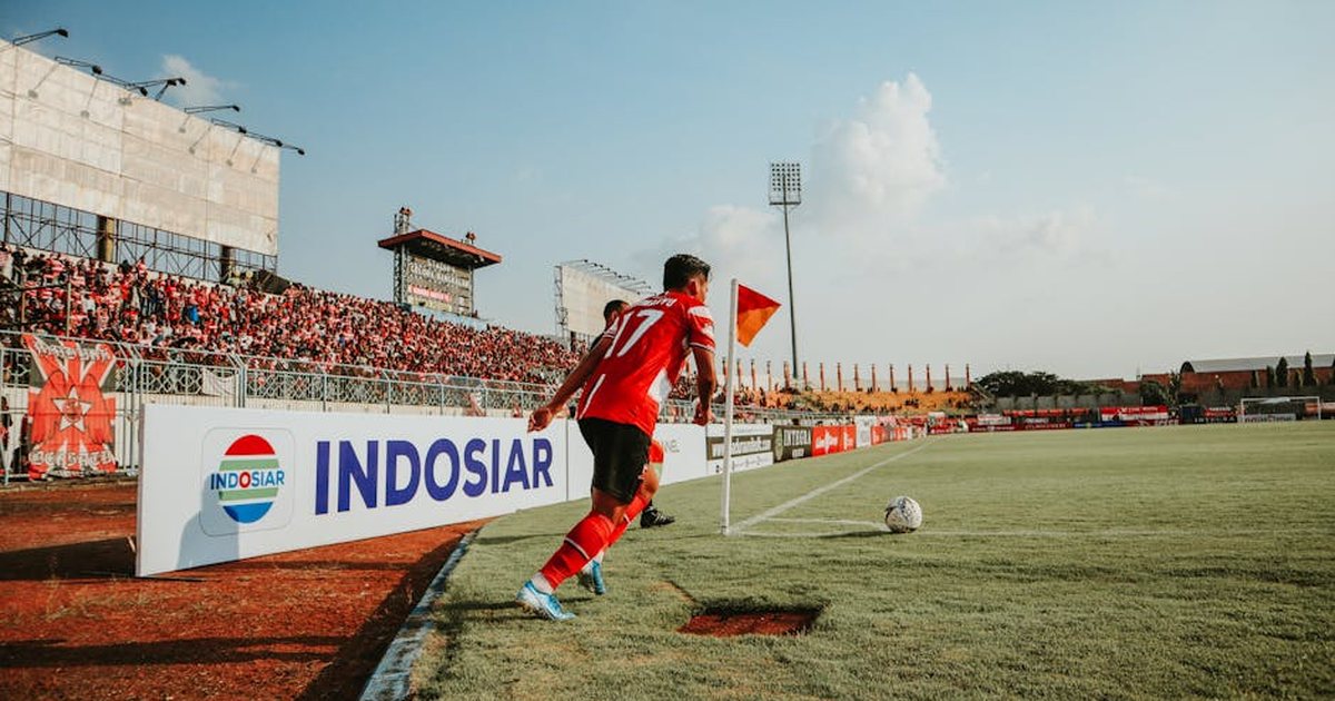 A football player takes a corner kick in a lively Indonesian stadium filled with fans.