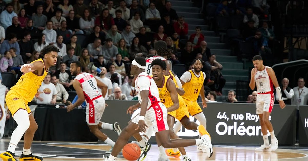 Players in action during an indoor basketball game, with a crowd watching intently.