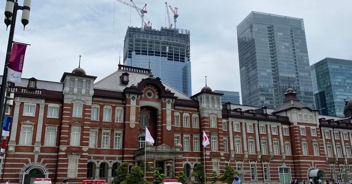 Tokyo Station's iconic facade with police cars and officers as skyscrapers loom in the background.