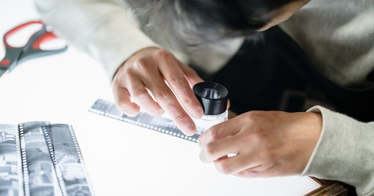 Photographer scrutinizing film negatives on a lightbox using a magnifying glass, focusing on details.
