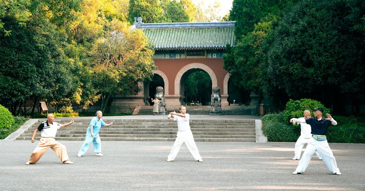 A group practicing Tai Chi near Linggu Temple in Nanjing, China, surrounded by lush green trees.