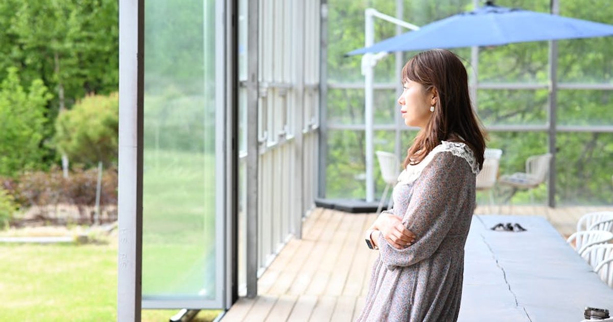 A serene moment of a woman enjoying the view from a porch on a sunny day, epitomizing relaxation.