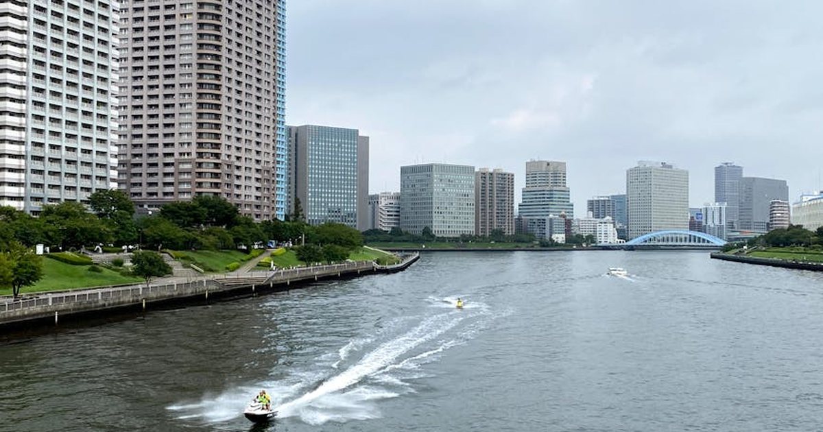 Aerial view of Tokyo waterfront featuring city skyline with motorboats on the river.