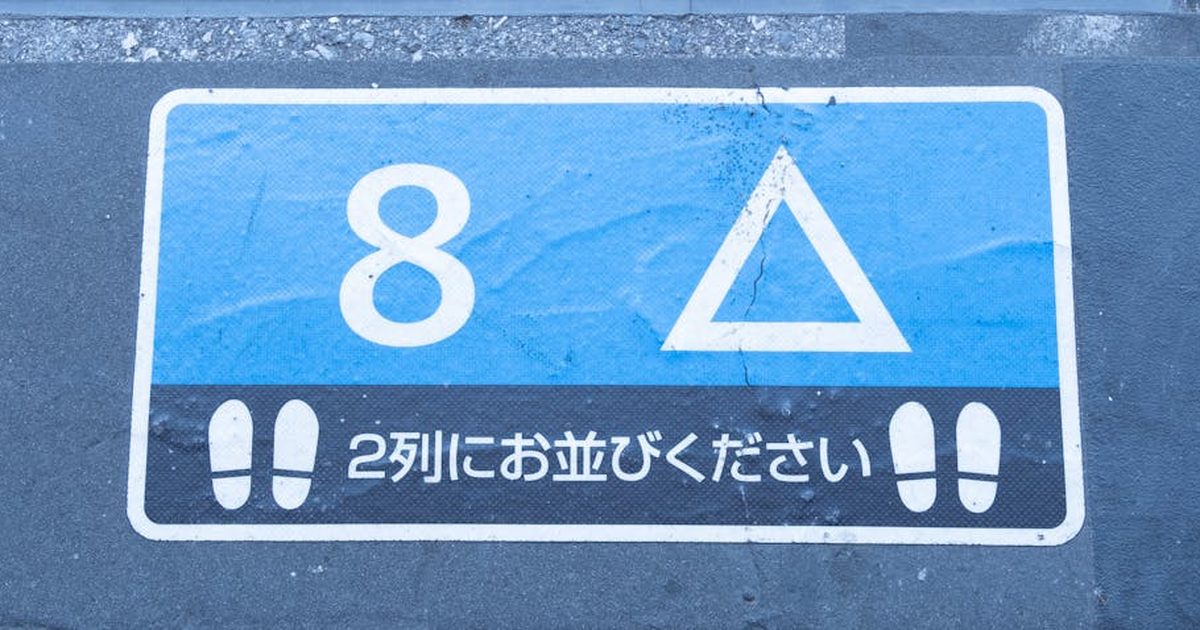 Blue and white queue sign with numbers and symbols on pavement in Japan.