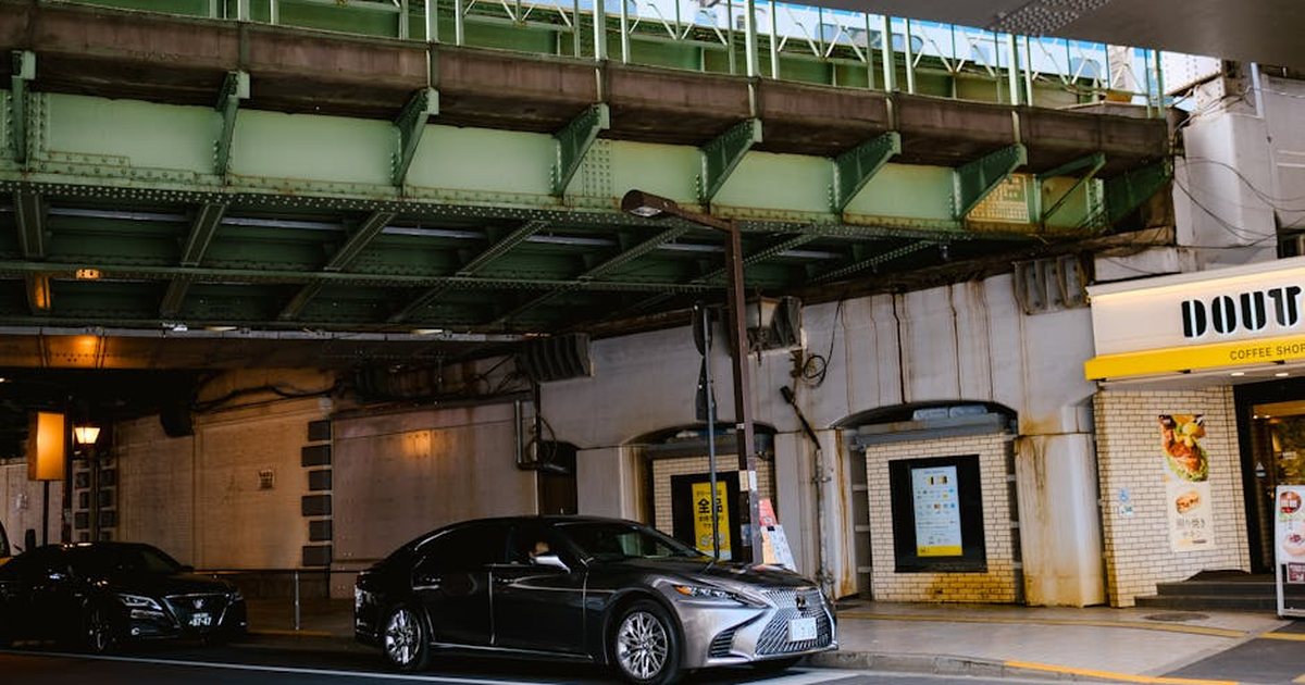 Cars parked under a green overpass bridge near a coffee shop entrance in the city.