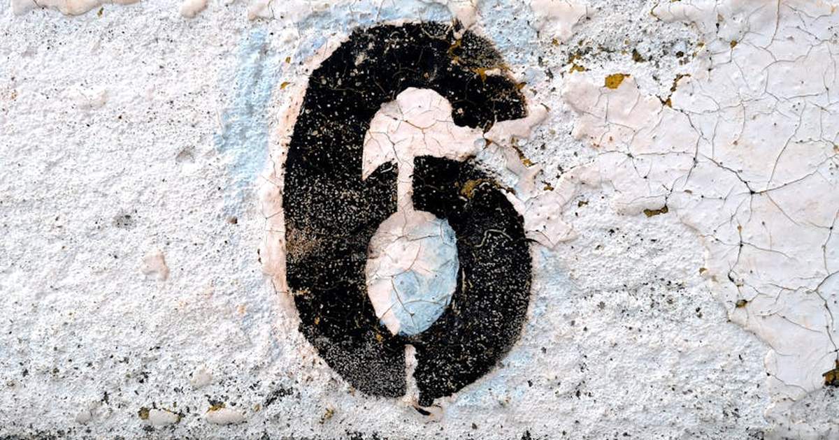 Close-up of a weathered number six painted on a cracked road surface.