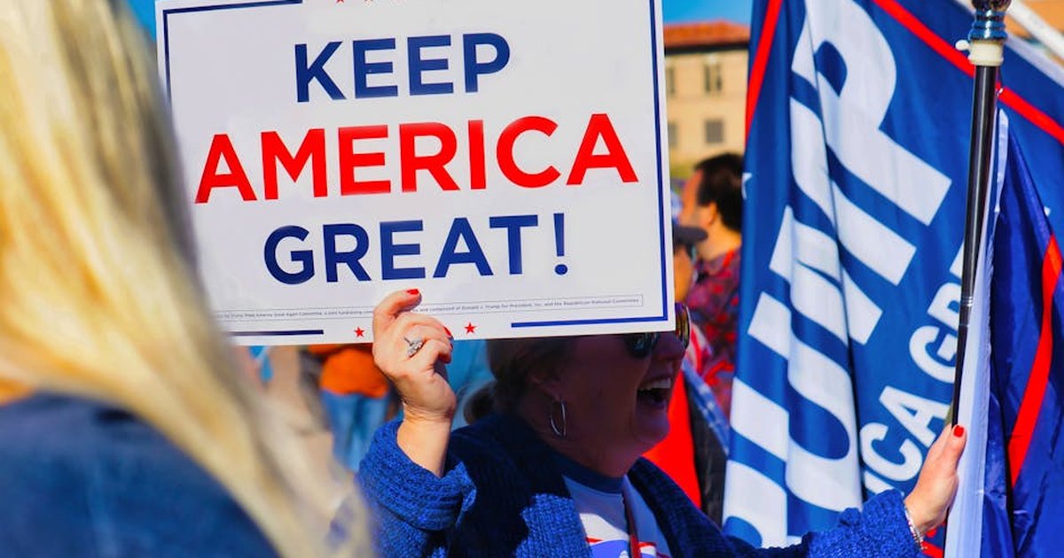 Crowd gathering in Phoenix holding 'Keep America Great' sign at political event outdoors.