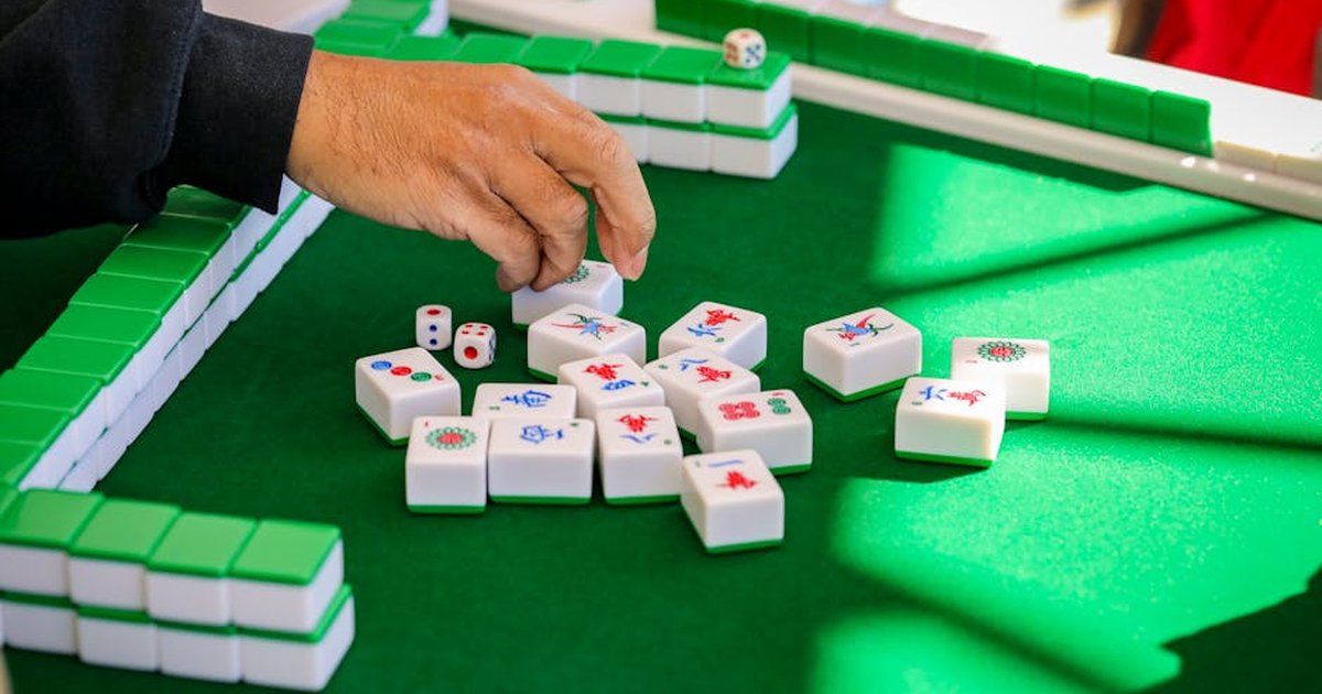 Hand arranging mahjong tiles during an intense game on a green table.