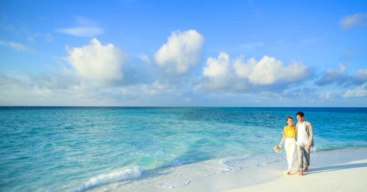 A couple enjoys a romantic stroll along a pristine tropical beach with turquoise waters.