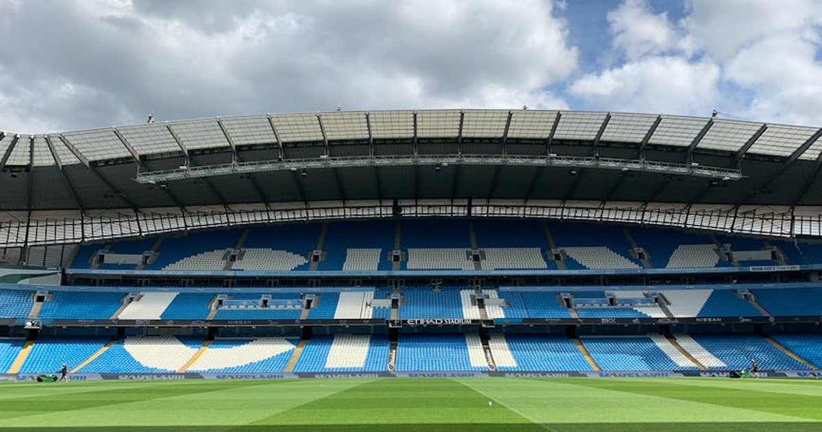 Etihad Stadium in Manchester with empty blue seats under a cloudy sky.
