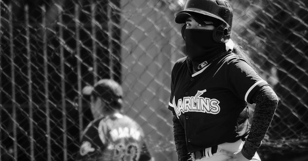 Unrecognizable baseball player in uniform wearing a helmet and facemask, captured in black and white.